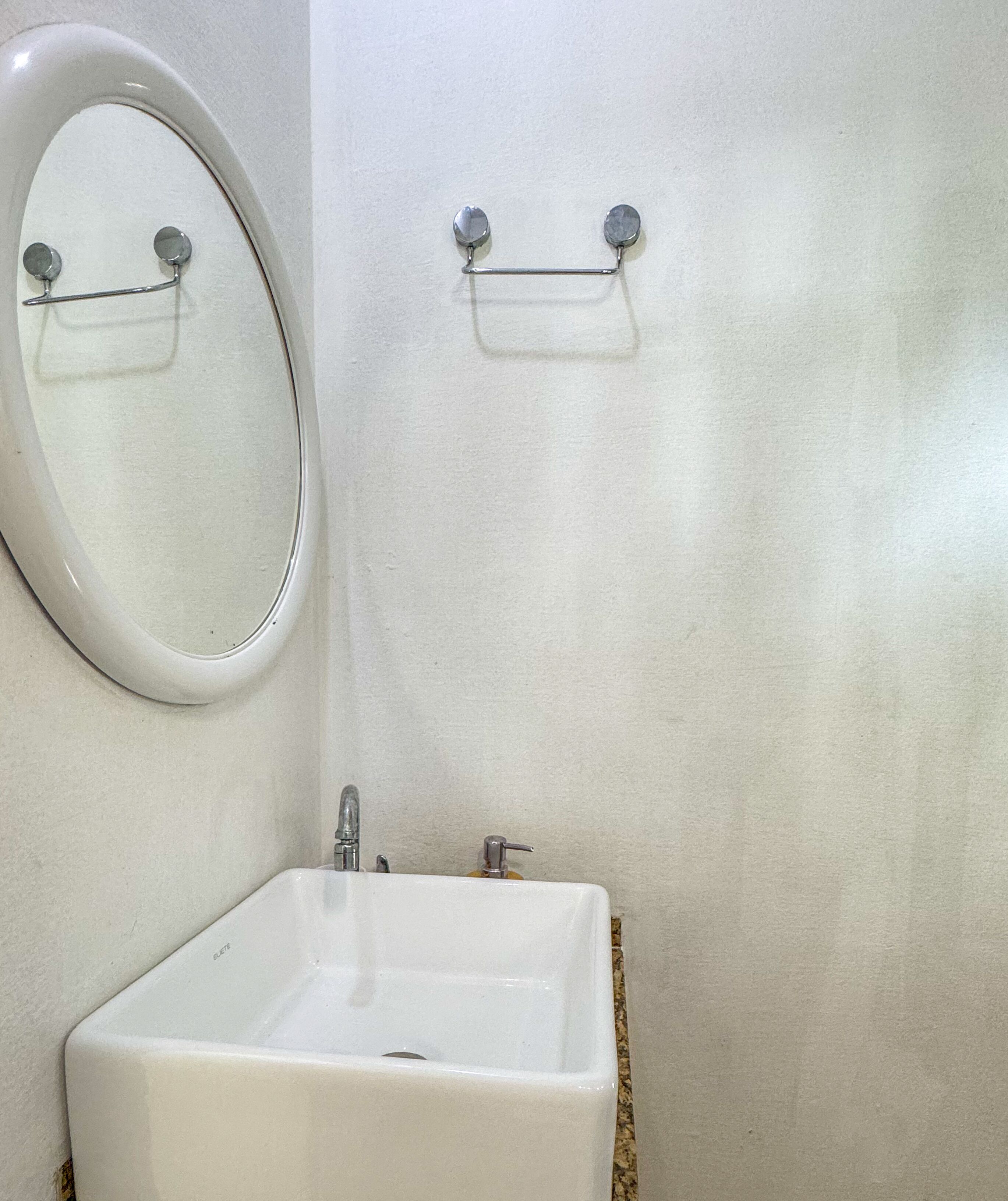 A bathroom with a white sink, a mirror, and a soap dispenser on the wall.