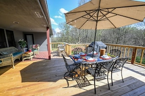 A deck with a table set for dining, outdoor furniture, and a grill.