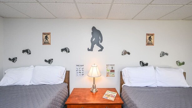 Habitación de hotel con dos camas, una mesita de noche con lámpara, y adhesivos murales que incluyen la silueta de un dinosaurio y huellas de animales.