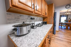 Eine Küche mit Holzausstattung, einer Granit-Arbeitsplatte, einem Slow Cooker, einem Mixer und einem Kühlschrank.