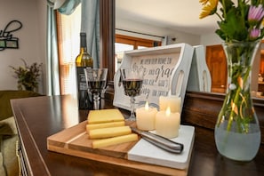 A wooden cutting board with cheese and a knife, a bottle of wine, two glasses, and a candle on a table.
