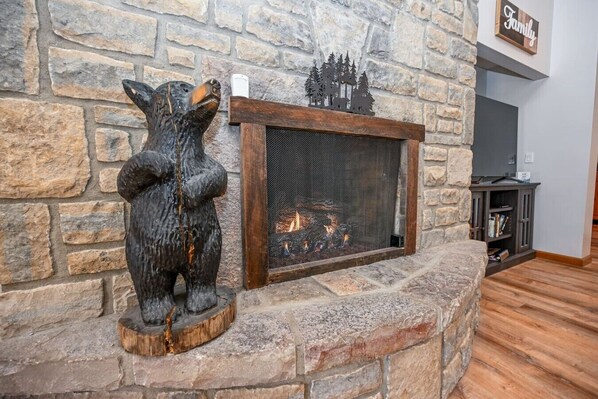 A stone fireplace with a bear sculpture and a forest silhouette decoration.