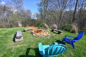 Ein Sitzbereich im Freien mit Feuerstelle, Bänken und Stühlen.