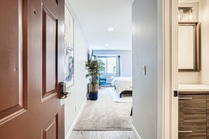 A hallway leading to a bedroom with a bed, a potted plant, and a bathroom with a mirror. - Modern DTC King Studio with Wet Bar, Pool, Light Rail (Greenwood Village)