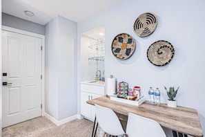 A kitchen with a wooden countertop, white chairs, a white door, and wall-mounted woven baskets.