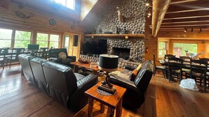 Ein geräumiges Blockhaus mit Kamin aus Stein, Ledersitzmöbeln und einem großen Fernseher.