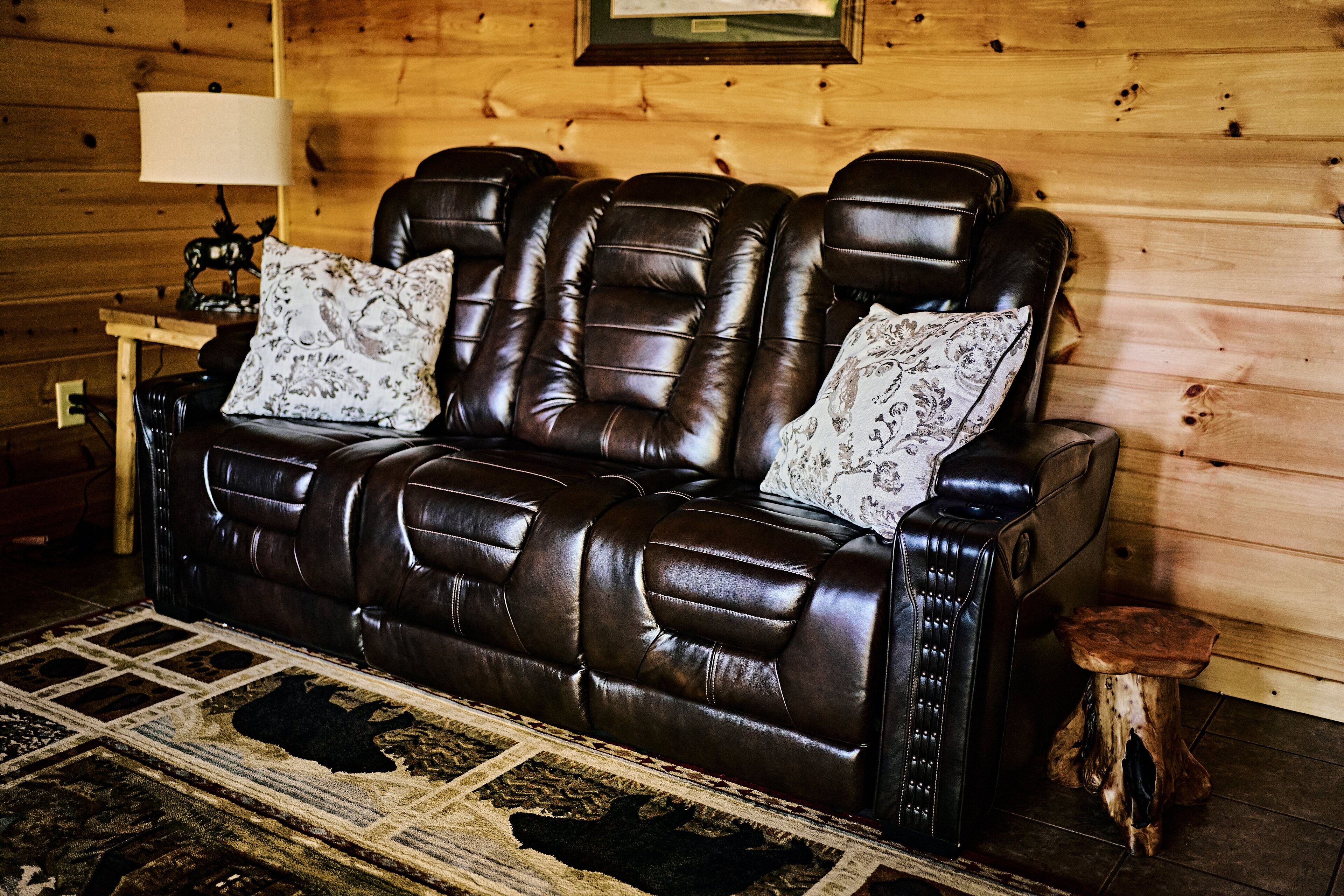 A brown leather sofa with floral cushions in a wooden cabin-style room.