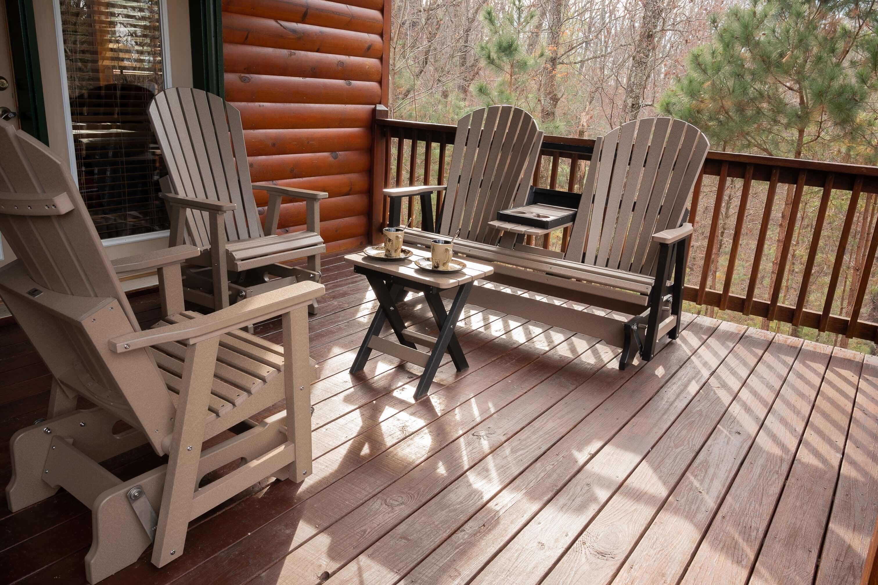Una terraza de madera con sillas Adirondack y una mesita, con vistas a un área boscosa.