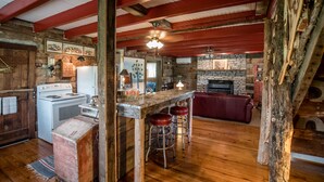 A rustic kitchen with wooden beams, a stone fireplace, and a bar area with stools.