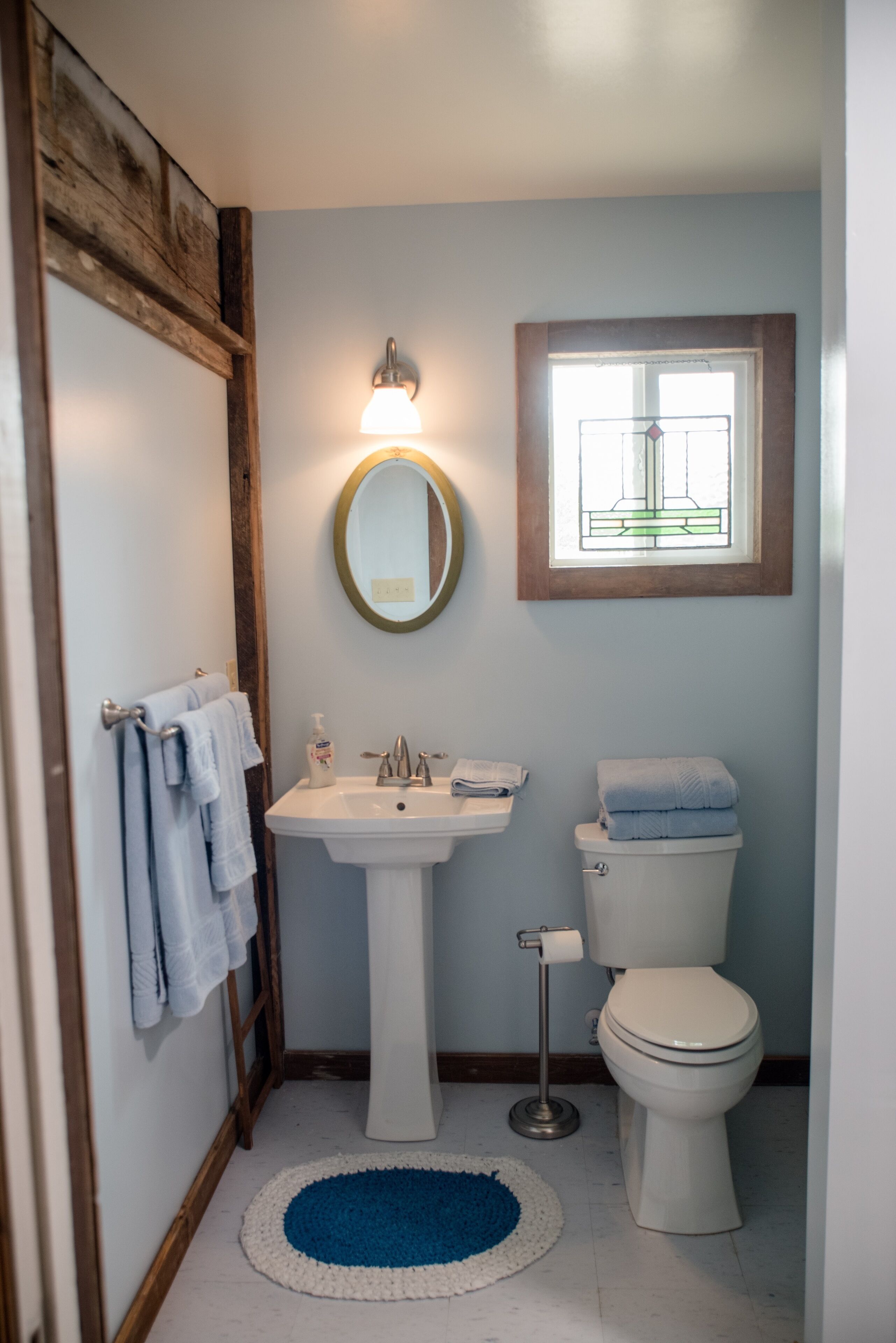 A bathroom with a pedestal sink, a toilet, and a window above the toilet.