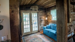 A rustic cabin interior with wooden walls, a blue sofa, and a large window.