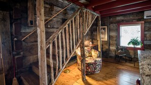 A rustic wooden staircase in a cabin-style room with a patterned armchair and a small table.
