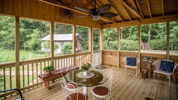 A covered outdoor deck with a round glass table, white metal chairs, and a ceiling fan.