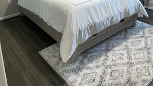 Ein Schlafzimmer mit einem Bett, einem Nachttisch, einer Lampe, einem Deckenventilator, einem Gemälde und einem gemusterten Teppich.