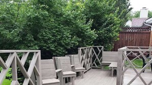 Eine Holzterrasse mit Stühlen und einer Bank, umgeben von einem Holzzaun und viel Grün.