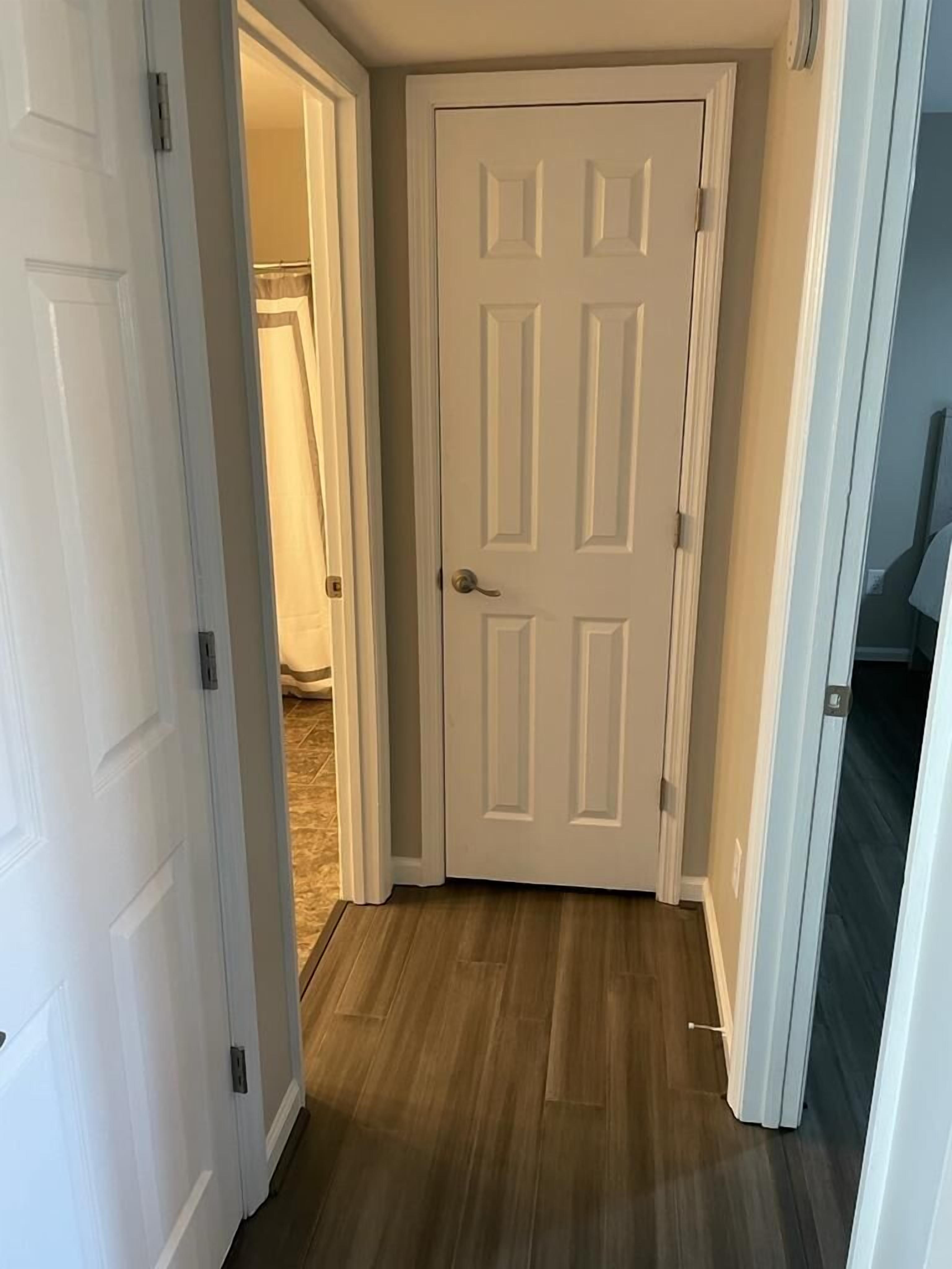 Un pasillo con una puerta blanca, suelo de madera y un armario con puerta corredera.