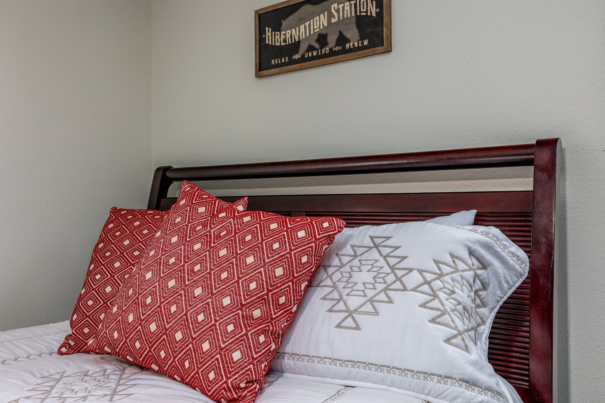 Una cama con cabecera de madera, dos almohadas estampadas y una señal sobre la cama.