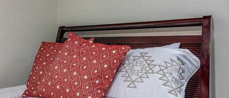 Una cama con cabecera de madera, dos almohadas estampadas y una señal sobre la cama.
