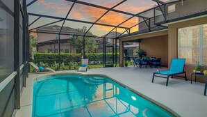 A swimming pool with a glass ceiling, surrounded by lounge chairs and a table with chairs.