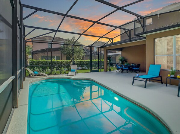 Una piscina con techo de vidrio, rodeada de sillas de descanso y una mesa con sillas.