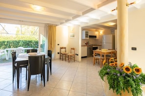 Un vaste espace de vie comprenant un coin repas avec table et chaises, une cuisine et un balcon offrant une vue sur la verdure.