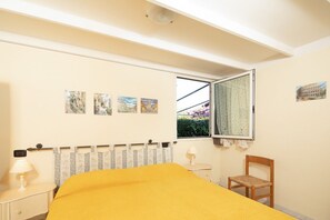 Une chambre à coucher comprenant un lit, une chaise, une table de chevet, une fenêtre et des œuvres d’art murales.