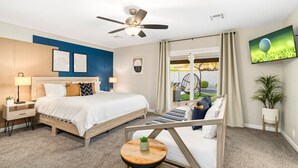 A hotel room with a bed, a desk, a ceiling fan, a TV, and a window with curtains. - Modern Cactus  - Heated Pool and Hot Tub (Peoria)