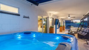 A hot tub area with a glass door leading to a room, a ceiling fan, and outdoor seating with a swing chair. - Modern Cactus  - Heated Pool and Hot Tub (Peoria)