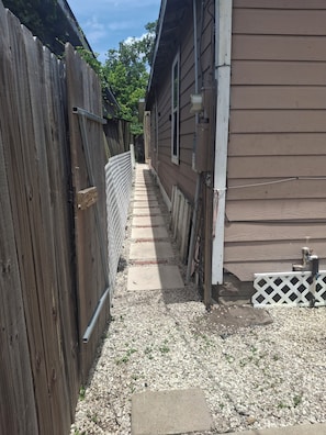 A narrow pathway leading to a wooden house with a white fence on one side and a white lattice fence on the other.