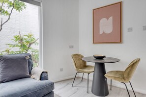 Una sala de estar moderna con un sofá gris, dos sillones, una mesa redonda con un cuenco y una obra de arte abstracto enmarcada en la pared.
