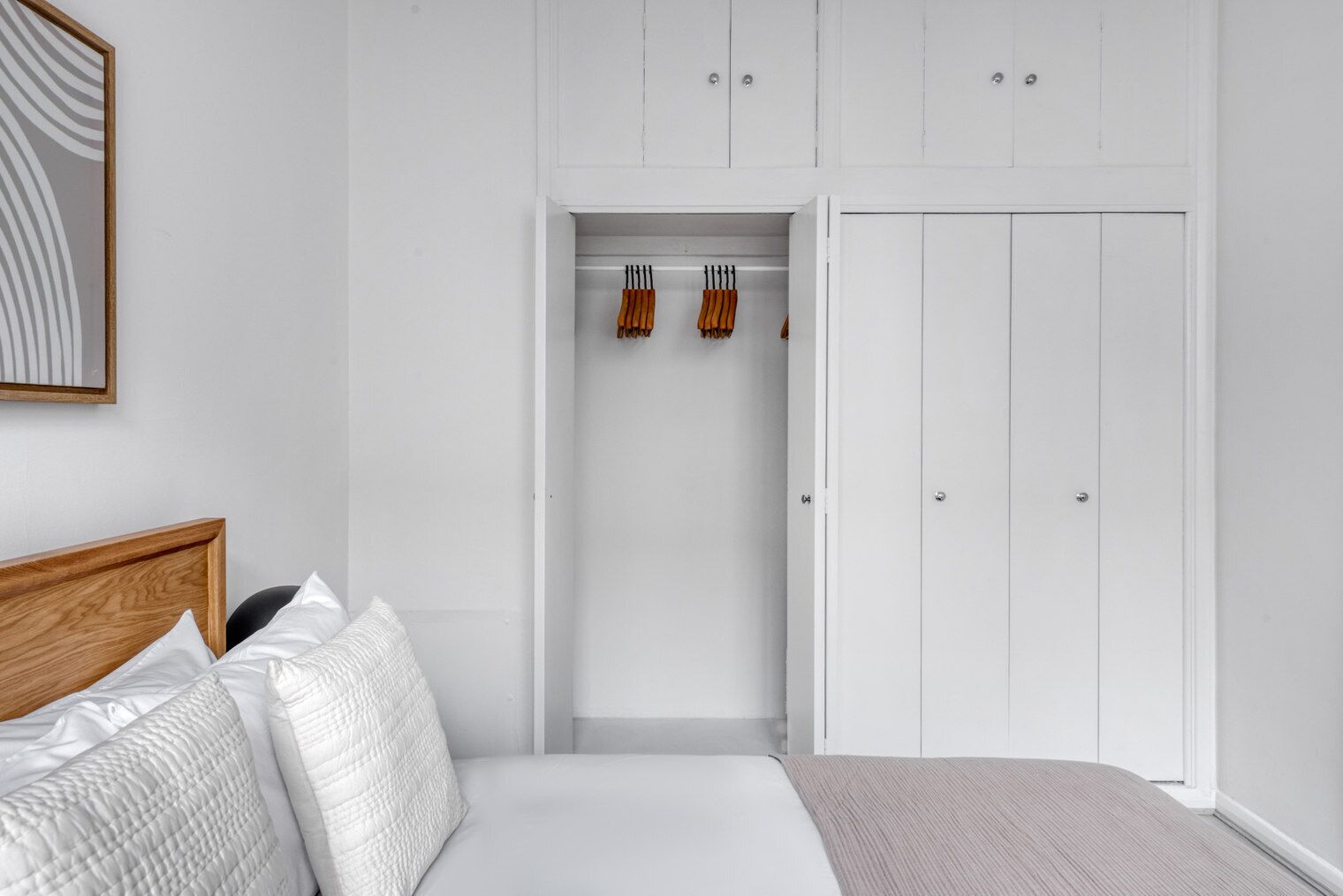 A bedroom with a bed, a wardrobe, and a hanging rack with tools.