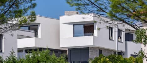 A modern multi-story building with balconies and large windows, surrounded by greenery.