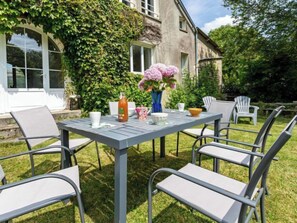 Un espace de restauration en plein air, avec une table et des chaises, entouré de verdure et bordé d’un bâtiment recouvert de lierre.
