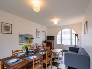 Un coin repas avec une table en bois dressée pour quatre personnes, entourée de chaises, d’un canapé bleu et d’un téléviseur posé sur un meuble.