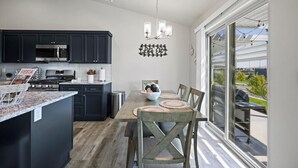A modern kitchen with dark cabinets, a stainless steel microwave, and a dining area with a wooden table and woven placemats. - New house!! Outdoor Hot tub with beautiful sunset views (Kennewick)