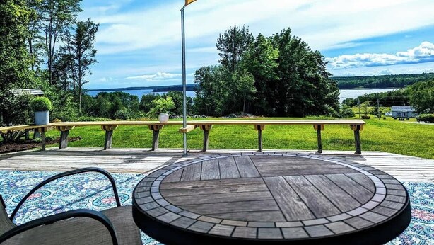 An outdoor patio with a round table and chairs, a wooden deck, and a view of a lake and trees. - Sunset Waterview Cottage w/Fire Pit Near Acadia (Ellsworth)