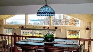 A dining area with a table, chairs, a hanging light fixture, and large windows with a view. - Sunset Waterview Cottage w/Fire Pit Near Acadia (Ellsworth)