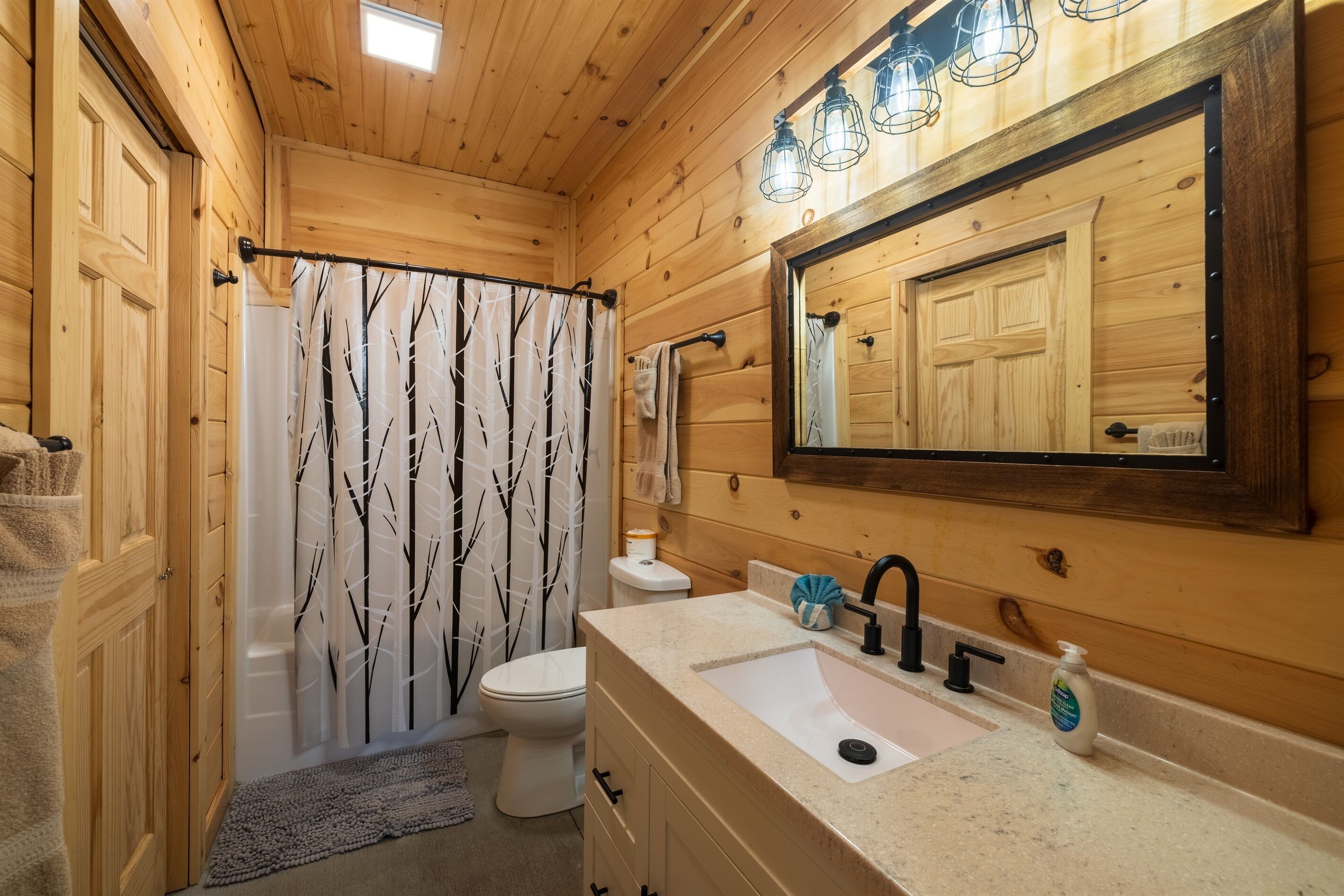 Une salle de bain rustique, aménagée dans une cabane en bois, avec des toilettes, un lavabo et un rideau de douche.