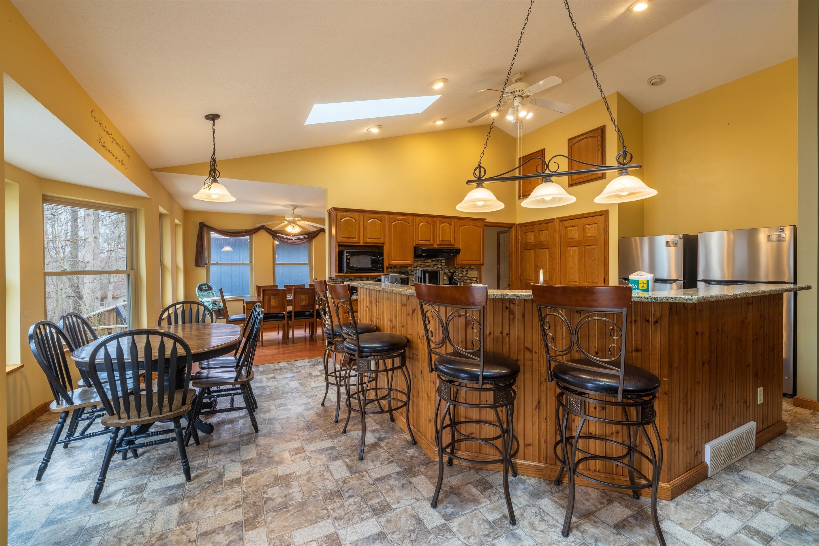 A kitchen with a central island, bar stools, wooden cabinets, and a dining area with chairs.