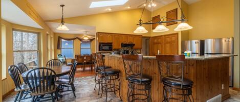 A kitchen with a central island, bar stools, wooden cabinets, and a dining area with chairs.