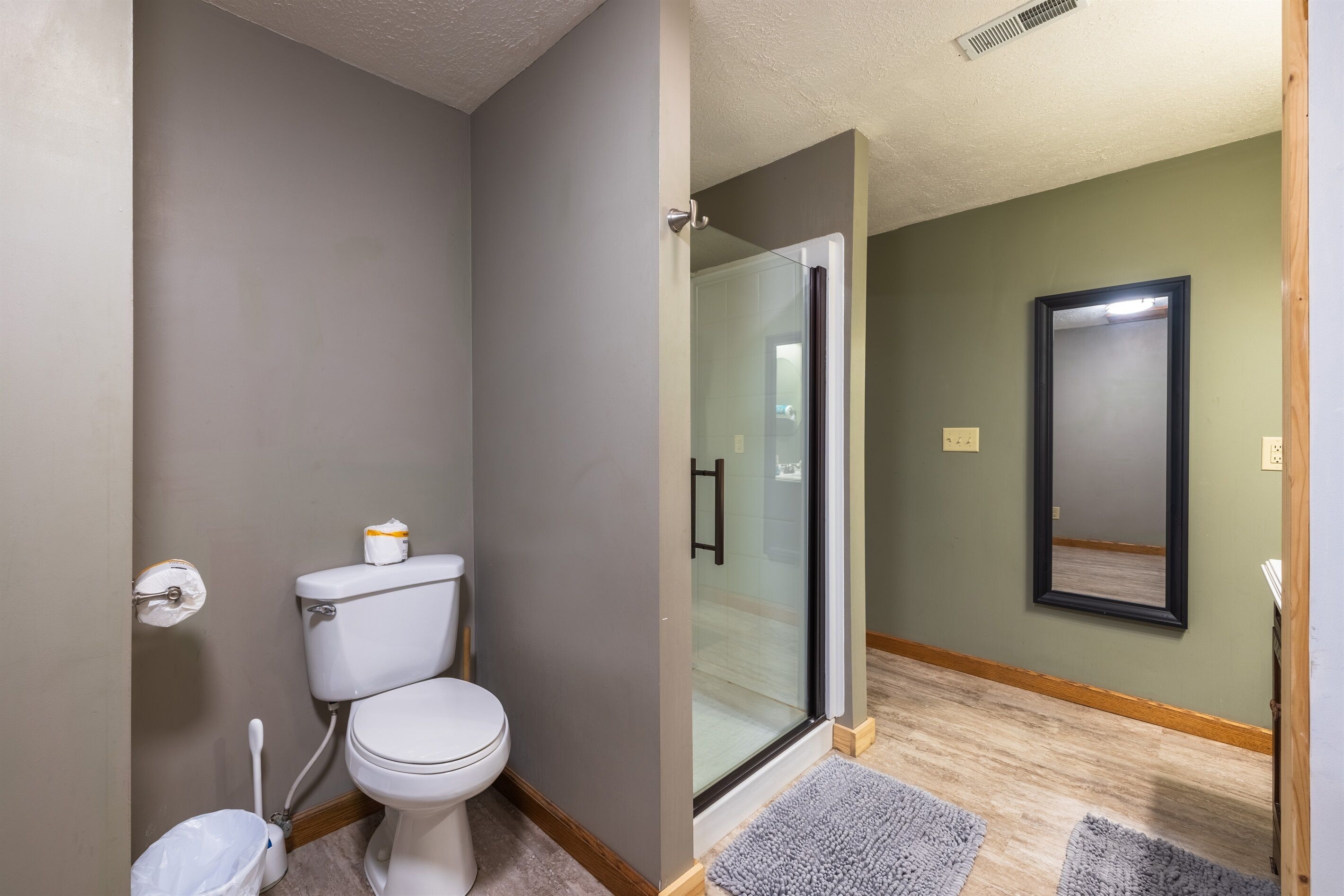 Une salle de bain comprenant des toilettes, une douche à parois de verre et un miroir mural.