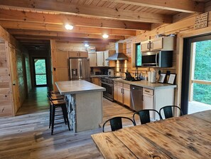 Interior de una cabaña de madera con cocina, comedor y vistas al exterior.
