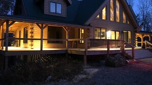 A log cabin with a porch and large windows, surrounded by trees.
