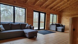 A spacious cabin with a wooden interior, large windows, a sectional sofa, and a smaller couch.