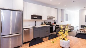 A modern kitchen with stainless steel appliances, grey cabinets, and a wooden dining table with chairs. - Vast and perfectly located 3 bedroom flat by Denstays (Montréal)