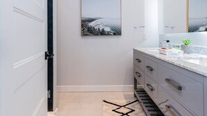 A modern bathroom with a marble vanity, a framed landscape picture on the wall, and a geometric rug on the floor. - Vast and perfectly located 3 bedroom flat by Denstays (Montréal)