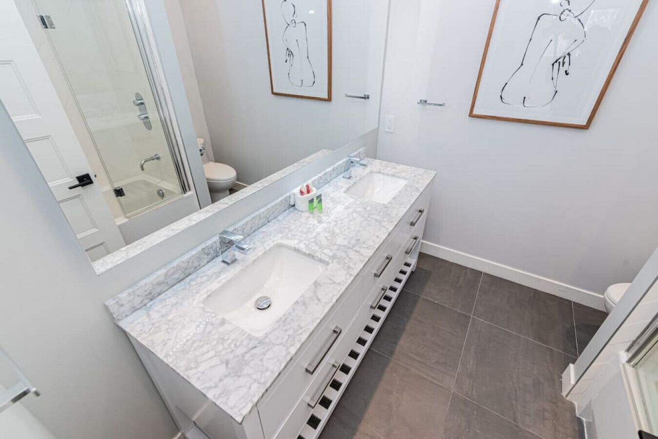 Une salle de bain moderne avec un double vasque, un grand miroir et des œuvres d’art accrochées aux murs.