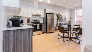 A modern kitchen with white cabinetry, stainless steel appliances, and a central island. There is a dining area with a table and chairs. - New classy 2 bedroom apartment in Le Plateau by Denstays (Montréal)