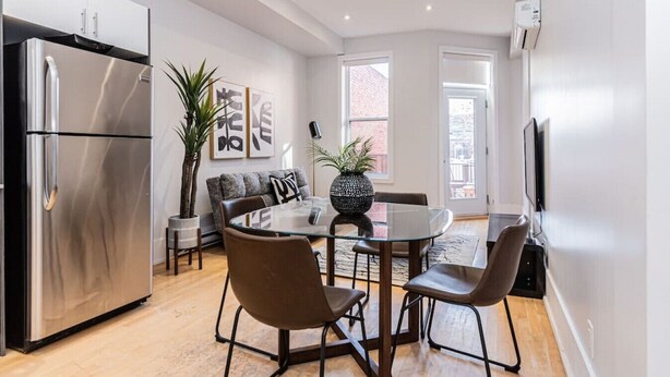 A modern kitchen with a stainless steel refrigerator, a dining table with chairs, a sofa, and a large potted plant. - New classy 2 bedroom apartment in Le Plateau by Denstays (Montréal)