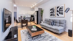 A modern living room with a sofa, coffee table, and a TV. There is a kitchen area with cabinets and appliances visible. - New classy 2 bedroom apartment in Le Plateau by Denstays (Montréal)